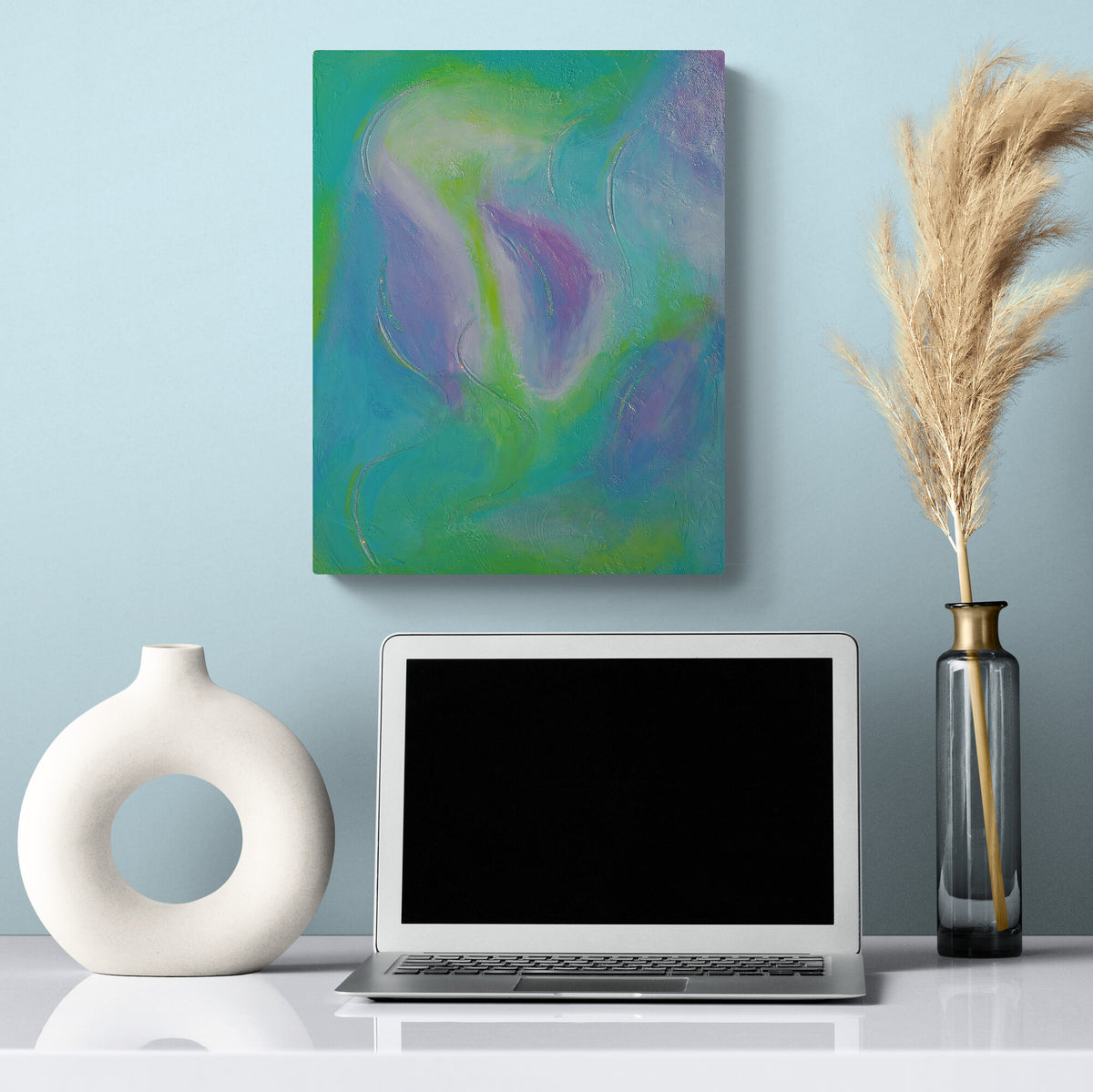 An abstract canvas art print with teal, green, and purple swirls hanging on a light blue wall above a desk setup with a laptop, a white ceramic vase, and a glass vase with dried pampas grass.